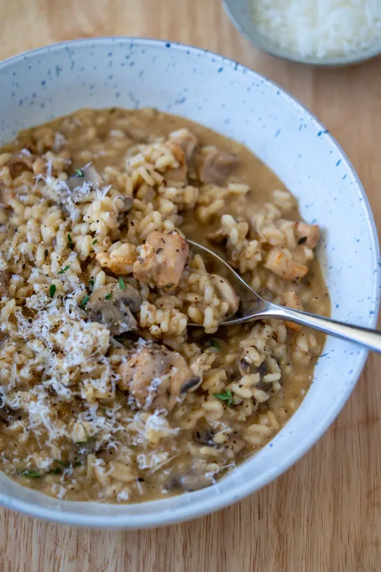 Creamy chicken and mushroom risotto topped with grated Parmesan and fresh herbs, served in a speckled bowl with a spoon.