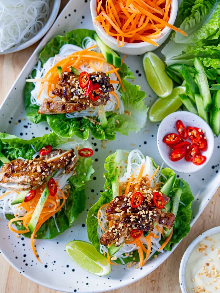 Top view of a full platter featuring hoisin chicken lettuce cups with vermicelli noodles, carrots, cucumber, crushed peanuts, and red chili, surrounded by fresh lime wedges, lettuce, and extra garnishes.