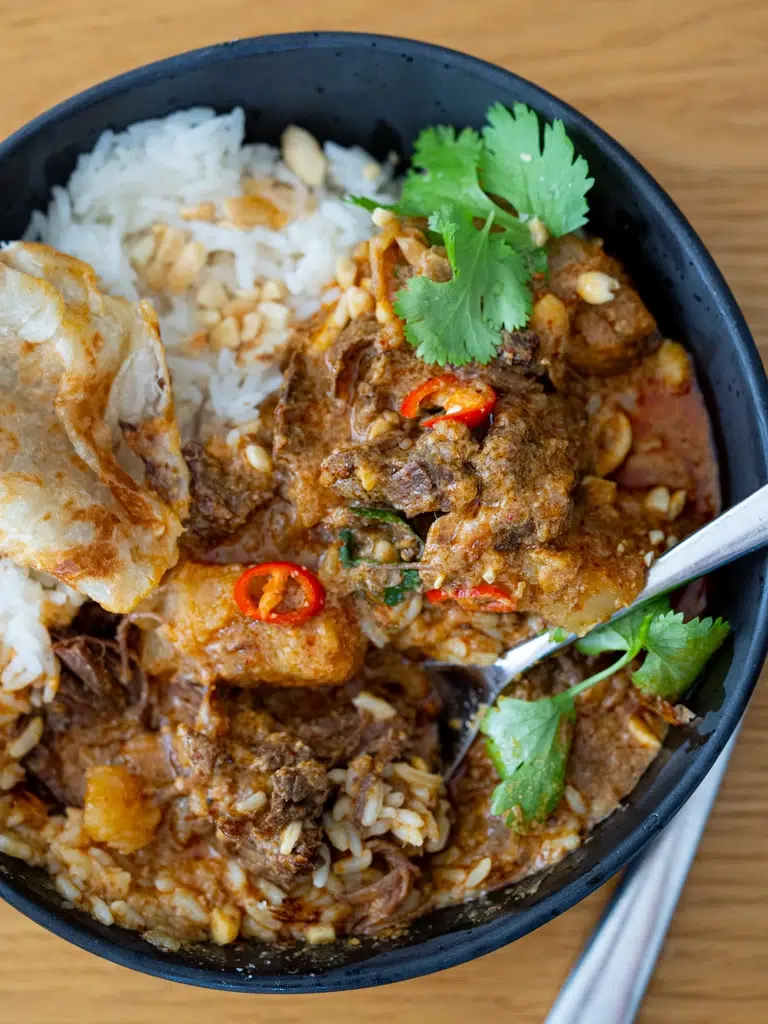 Massaman beef curry plated with rice, a spoon digging into the bowl