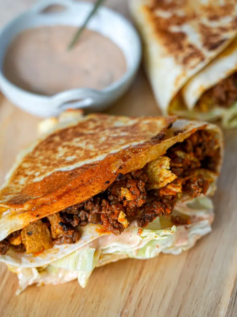 Close-up of folded nacho wraps filled with seasoned meat and cheese, grilled to a crispy golden brown, served on a wooden board