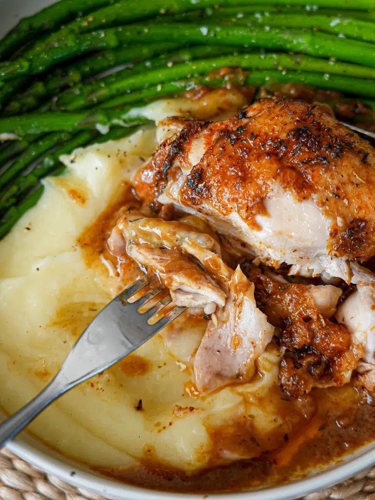 Baked chicken and gravy with a fork slicing into tender meat, served with greens and mashed potatoes