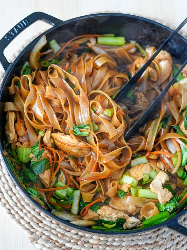 Close-up of Drunken Noodles in a pan with tongs for serving