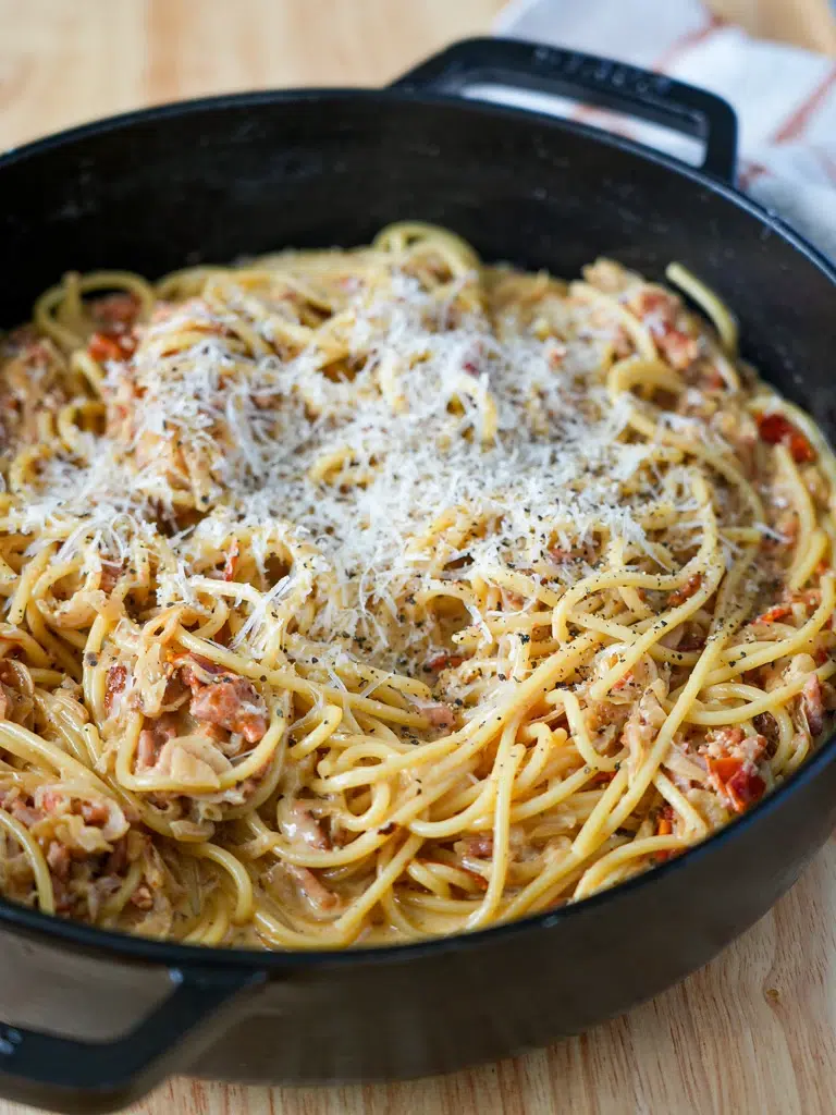 Cooked pasta in a black pan, ready to serve, viewed from the side.