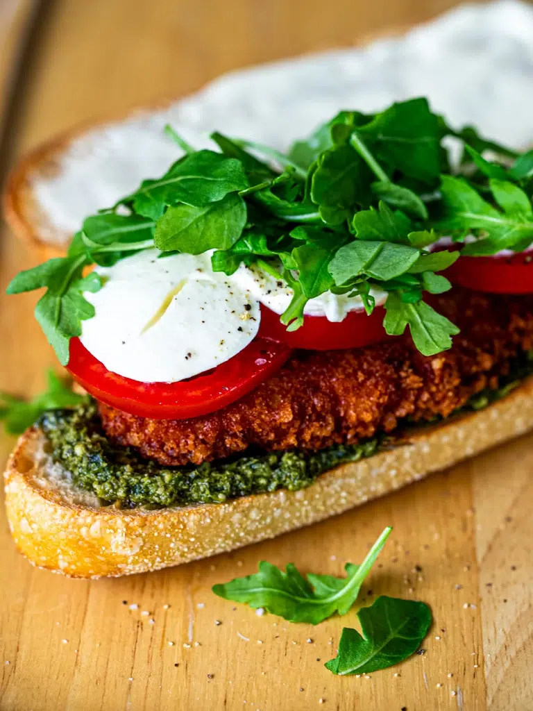 Open crispy chicken pesto sandwich showing layered ingredients on toasted bread.