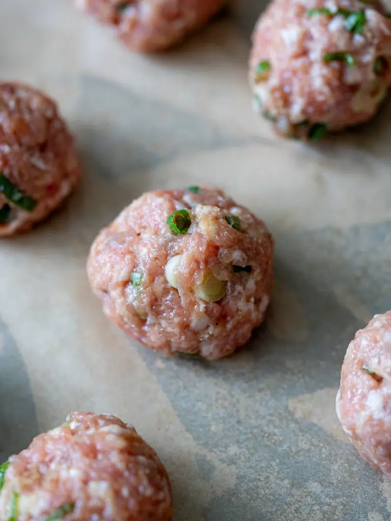 Rolled pork meatballs arranged neatly on a tray, ready to cook.