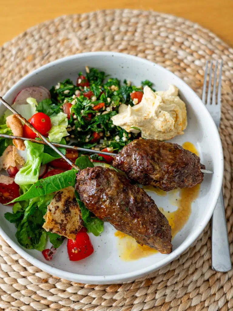Plated lamb kofta alongside vibrant fattoush salad and creamy hummus.