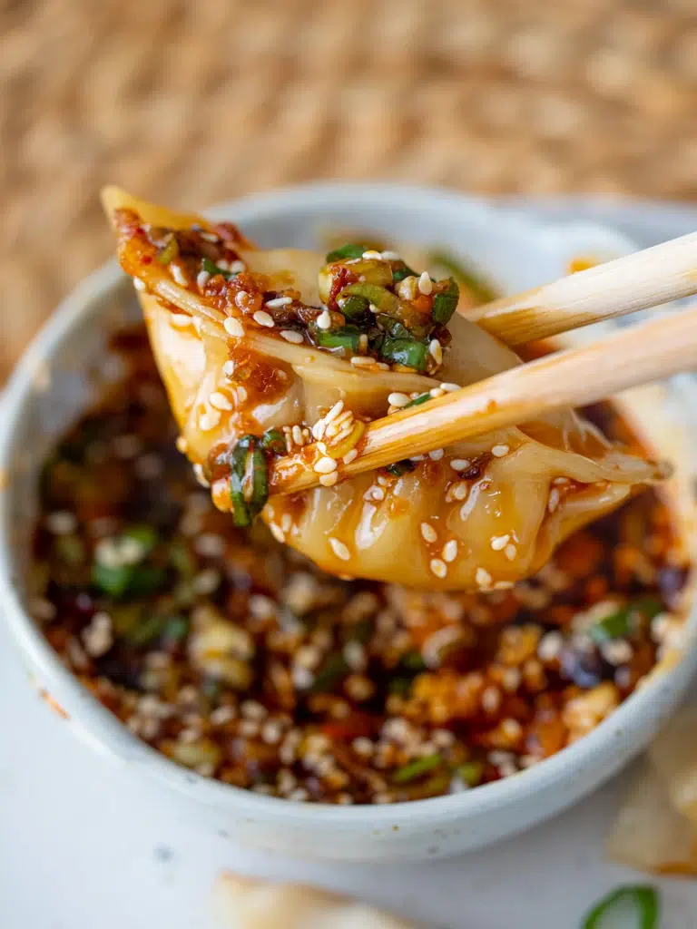 dumpling just dunked in sauce being held by chopsticks