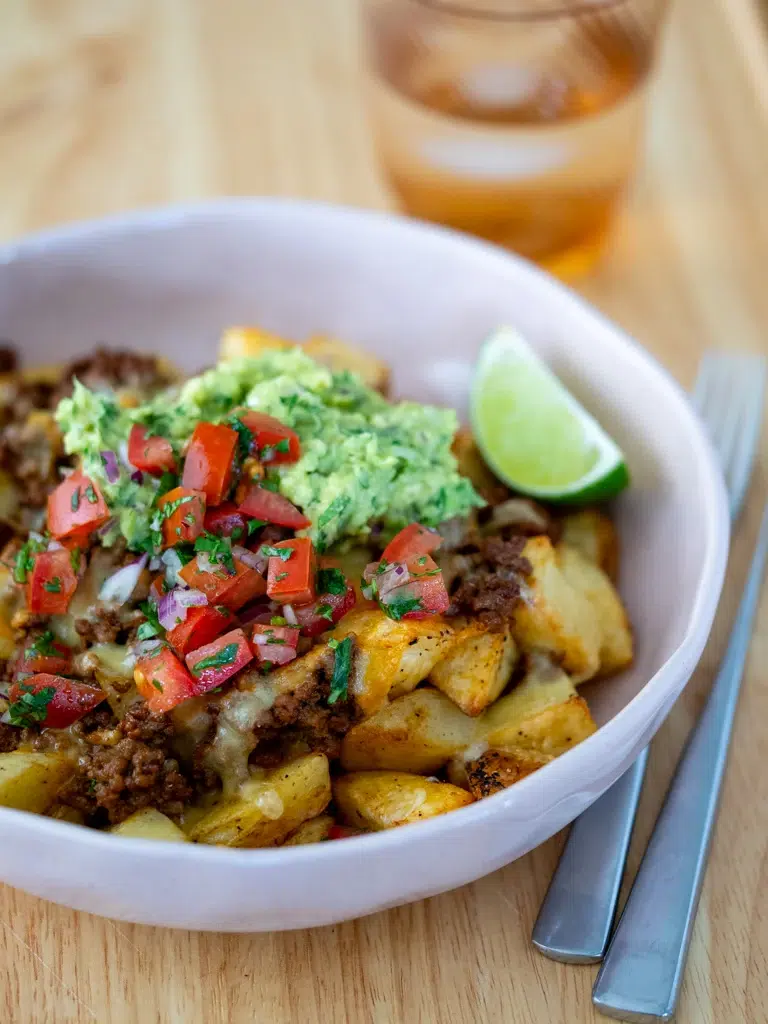 Side view close-up of a potato taco bowl served in a white bowl with a fork on the side.