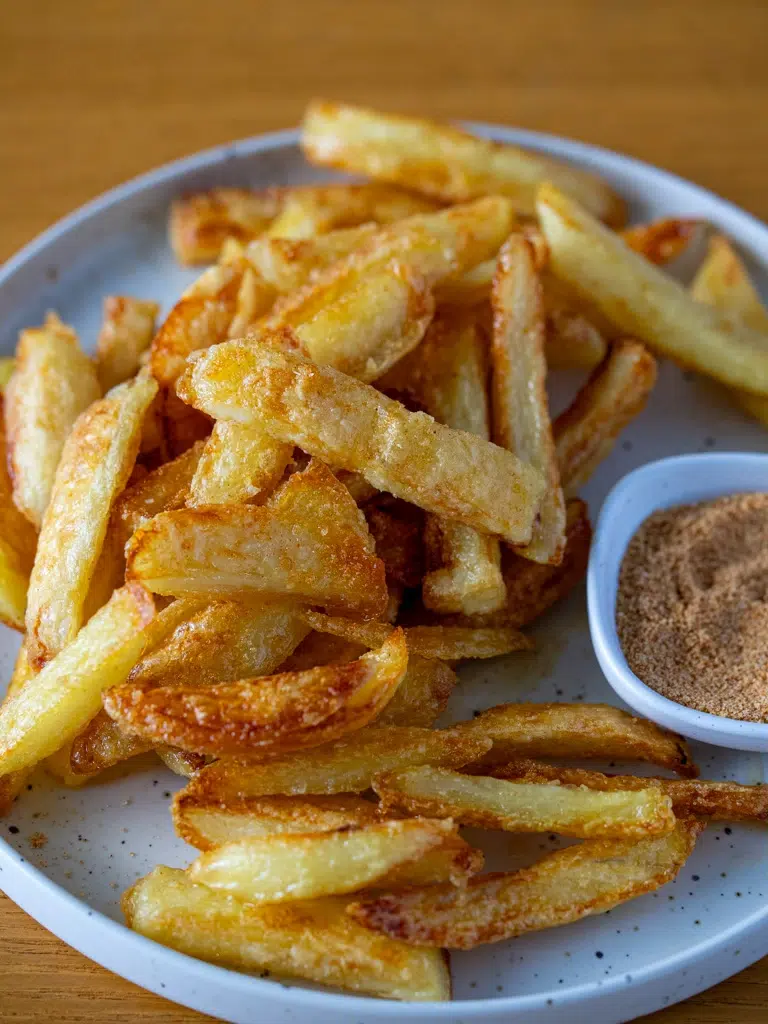 Crispy golden oven fries served with a small dish of chicken salt seasoning on a white plate