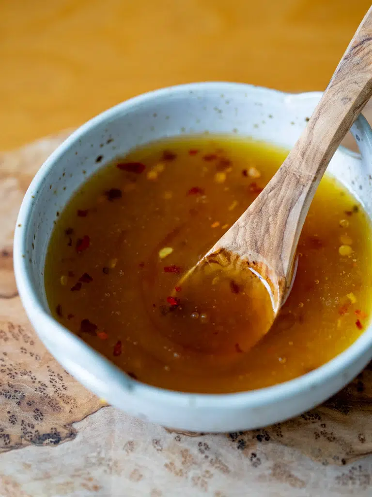 Close-up of easy hot honey sauce with chili flakes in a ceramic bowl, stirred with a wooden spoon.