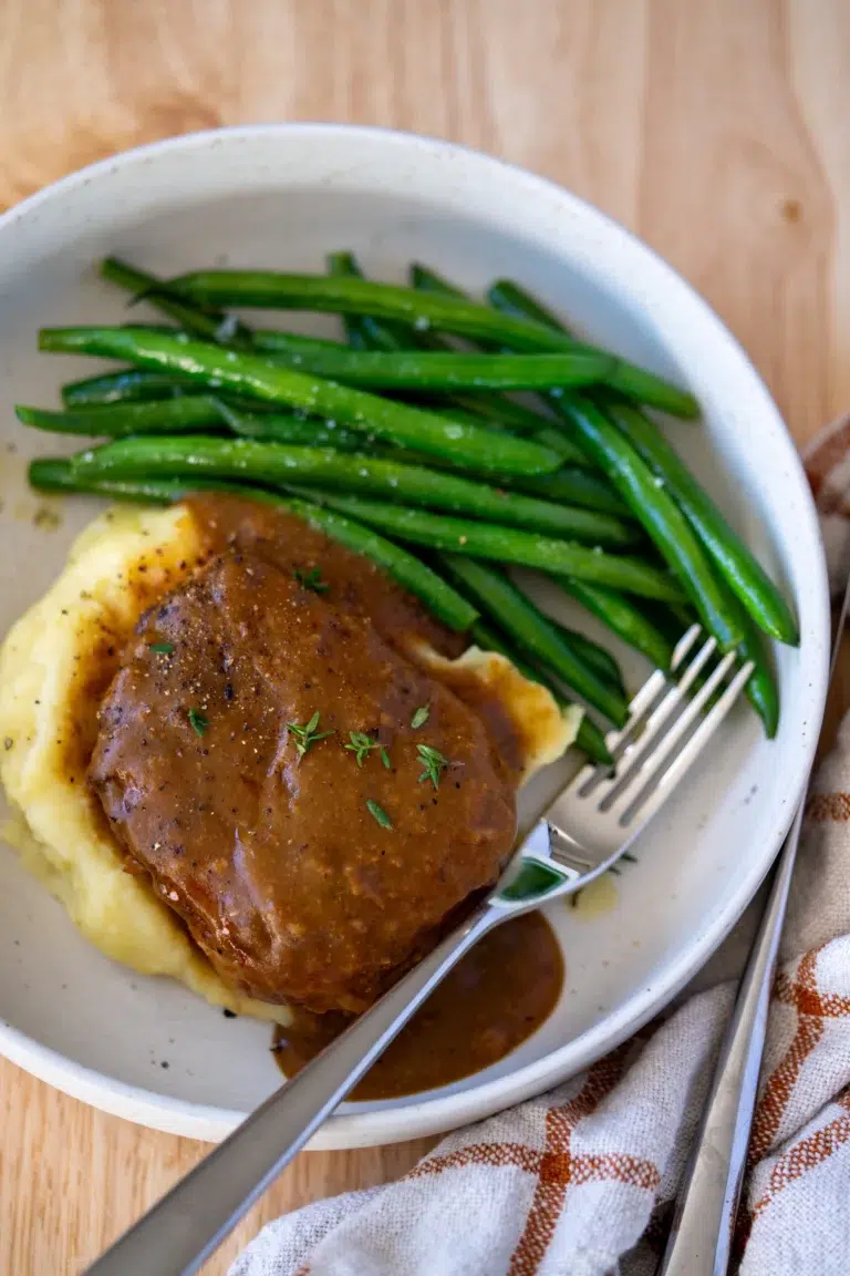 Overhead shot of pork chop with homemade gravy, mashed potatoes, and green beans – comforting final plated dish
