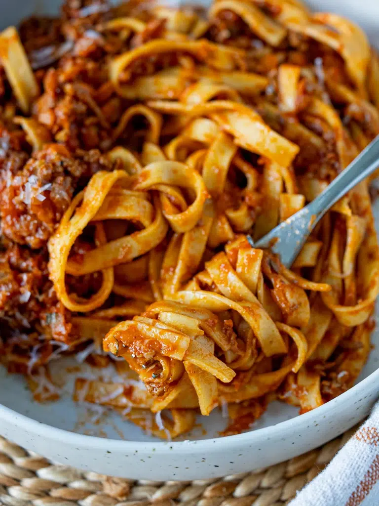 Close-up of fettuccine pasta tossed in a rich hidden vegetable Bolognese sauce, served in a white ceramic bowl with a fork twirled into the noodles.