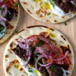 Platter of oven-baked kebabs served with flatbreads, garlic yoghurt, sumac onions, tomatoes, and fresh herbs for assembling wraps