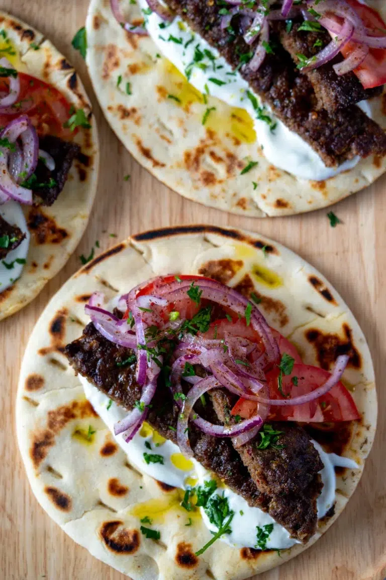 Platter of oven-baked kebabs served with flatbreads, garlic yoghurt, sumac onions, tomatoes, and fresh herbs for assembling wraps