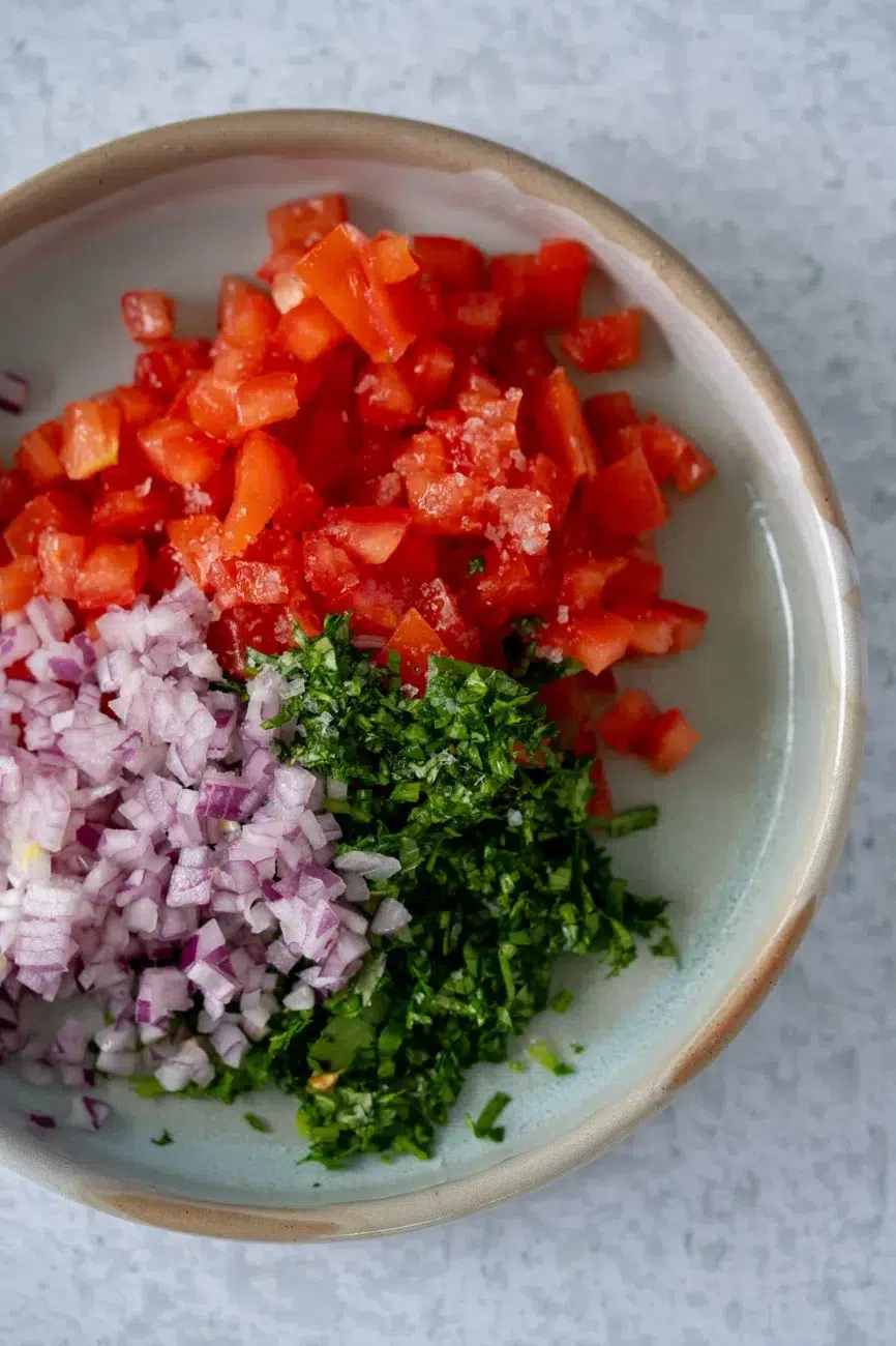 Bowl of pico de gallo ingredients — chopped tomatoes, red onion, chili, coriander, lime, and salt — ready to be stirred