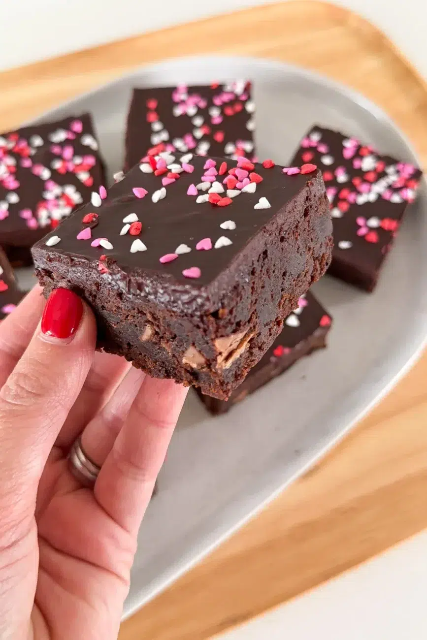Finished Valentines Day brownie being held in hand above the platter of brownies