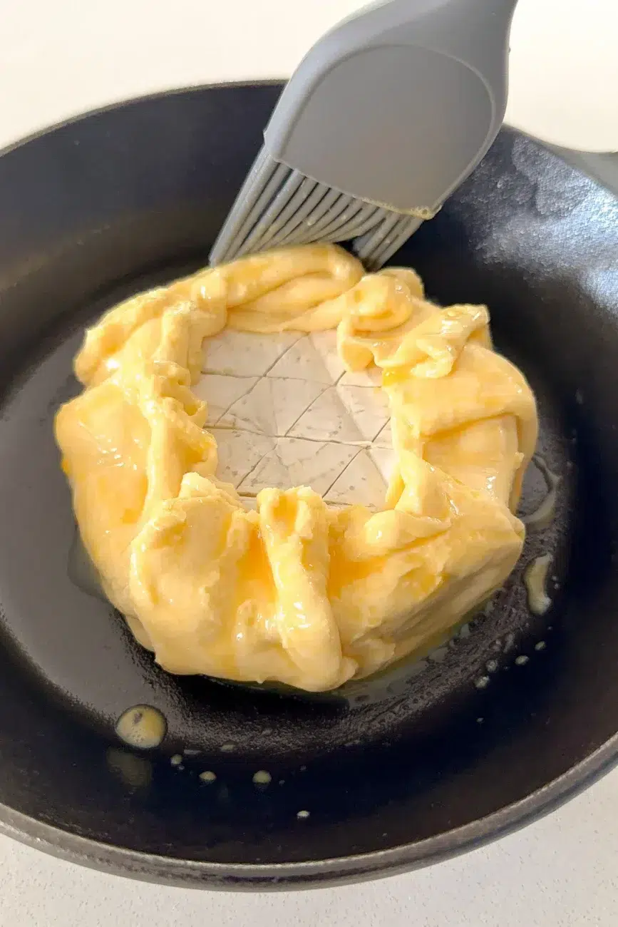 Brie encased in pastry being brushed with egg wash